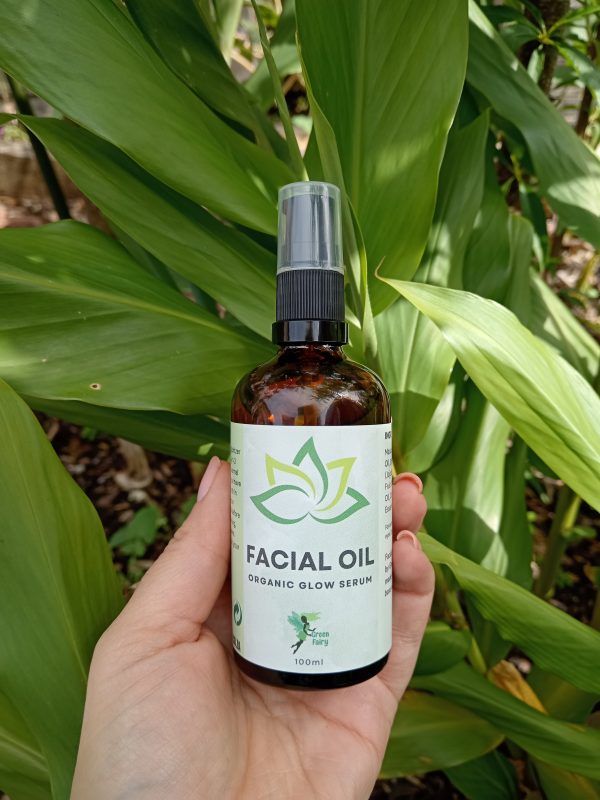 Facial Oil Organic Glow Serum held in a hand with a leaf background