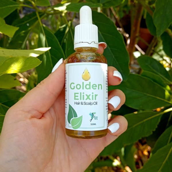 Manicured hands with white nails holds a bottle of Golden Elixir Hair and scalp oil